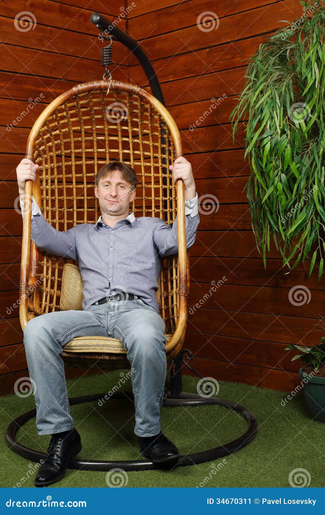 happy-man-sits-wicker-hanging-chair-near-wooden-wall-house-34670311.jpg